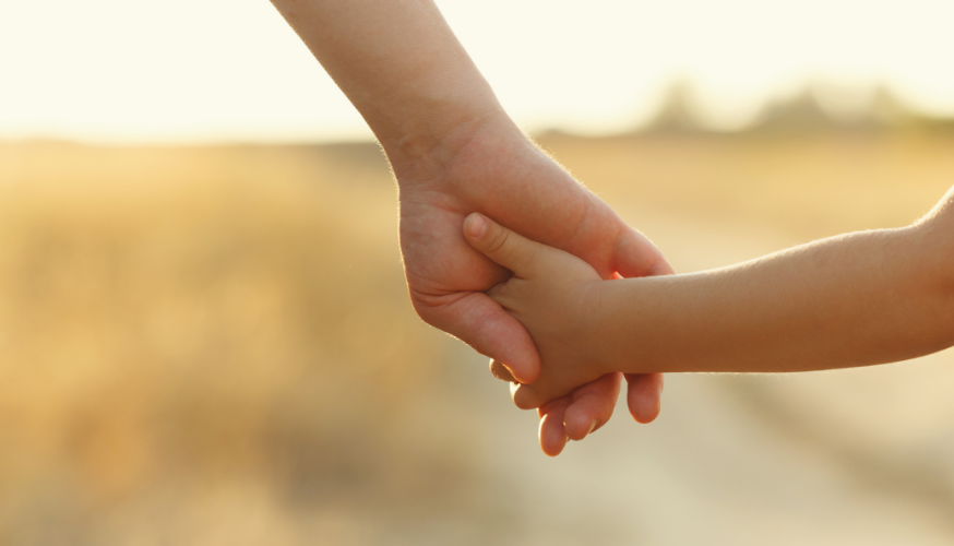 Ein Kind und ein Elternteil halten sich liebevoll die Hände inmitten der Natur.