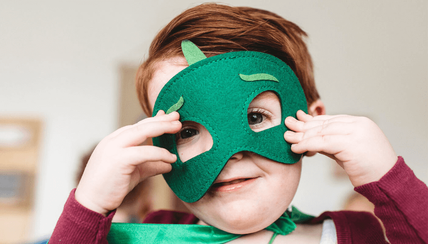 Ein verkleidetes Kind hält sich eine grüne Maske vor das Gesicht.