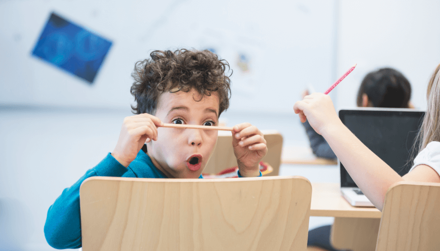 Ein Kind sitzt im Klassenzimmer und hält erstaunt einen Stift vor die Augen.