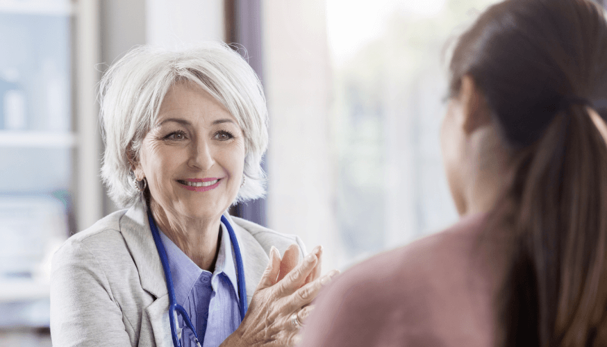 Lächelnde ältere Ärztin im Gespräch mit einer Patientin.