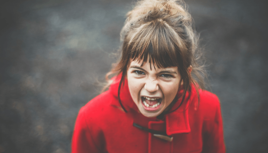 Breitformatiges Bild eines kleinen Mädchens mit aufgerissenen Augen und Mund, das in einem roten Mantel aggressiv brüllt, mit unscharfem dunklen Hintergrund.